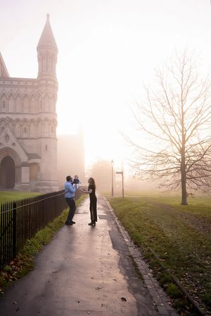 A couple shares a romantic moment on a misty morning path beside a gothic cathedral in autumn.
