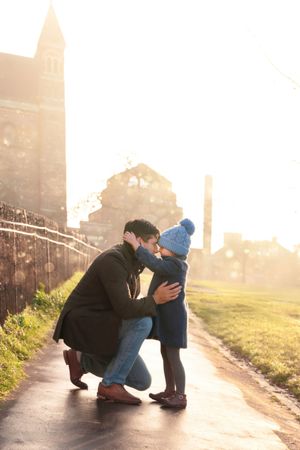 A Daddy, Daughter moment share a tender moment at sunset on a misty path with golden light filtering through the fog.