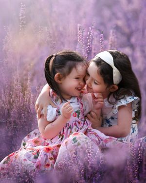 Two young children in floral dresses share a tender moment while sitting among blooming purple lavender flowers.