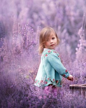 Child in a turquoise floral sweater standing in a dreamy purple Heather field on a misty day.