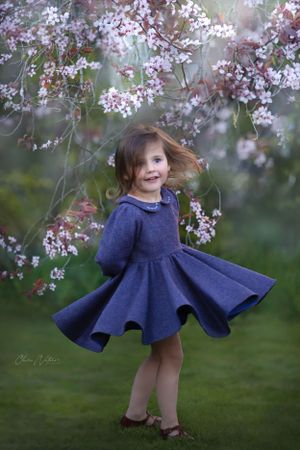 A twirling navy blue dress flows beneath blooming cherry blossoms in a spring garden scene.