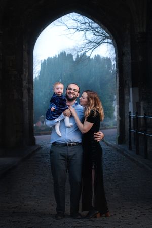Family poses together under stone archway during outdoor photo session at dusk.