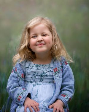 little blonde girl making a silly face laughing, whilst sat in nature surrounded by beautiful flowers.