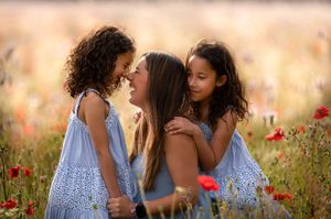 Children in matching blue dresses among red poppies and wildflowers at sunset.
