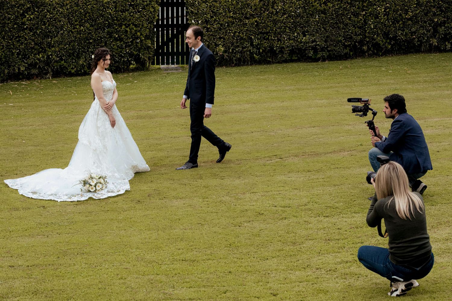 Wedding photographers capture shots of a bride and groom on a manicured lawn.