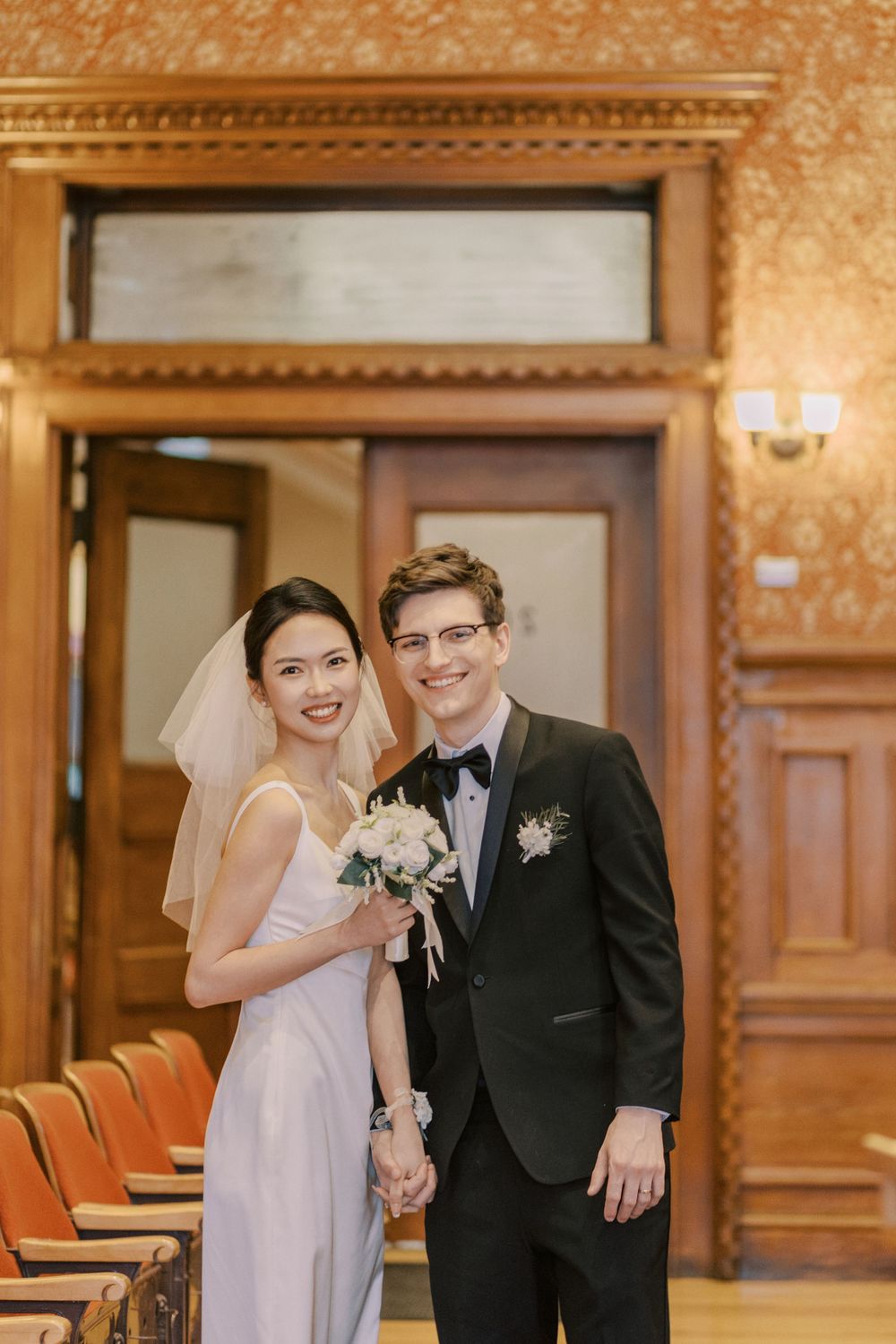 A joyful wedding couple shares a candid moment in an elegant wood-paneled room with ornate wallpaper.