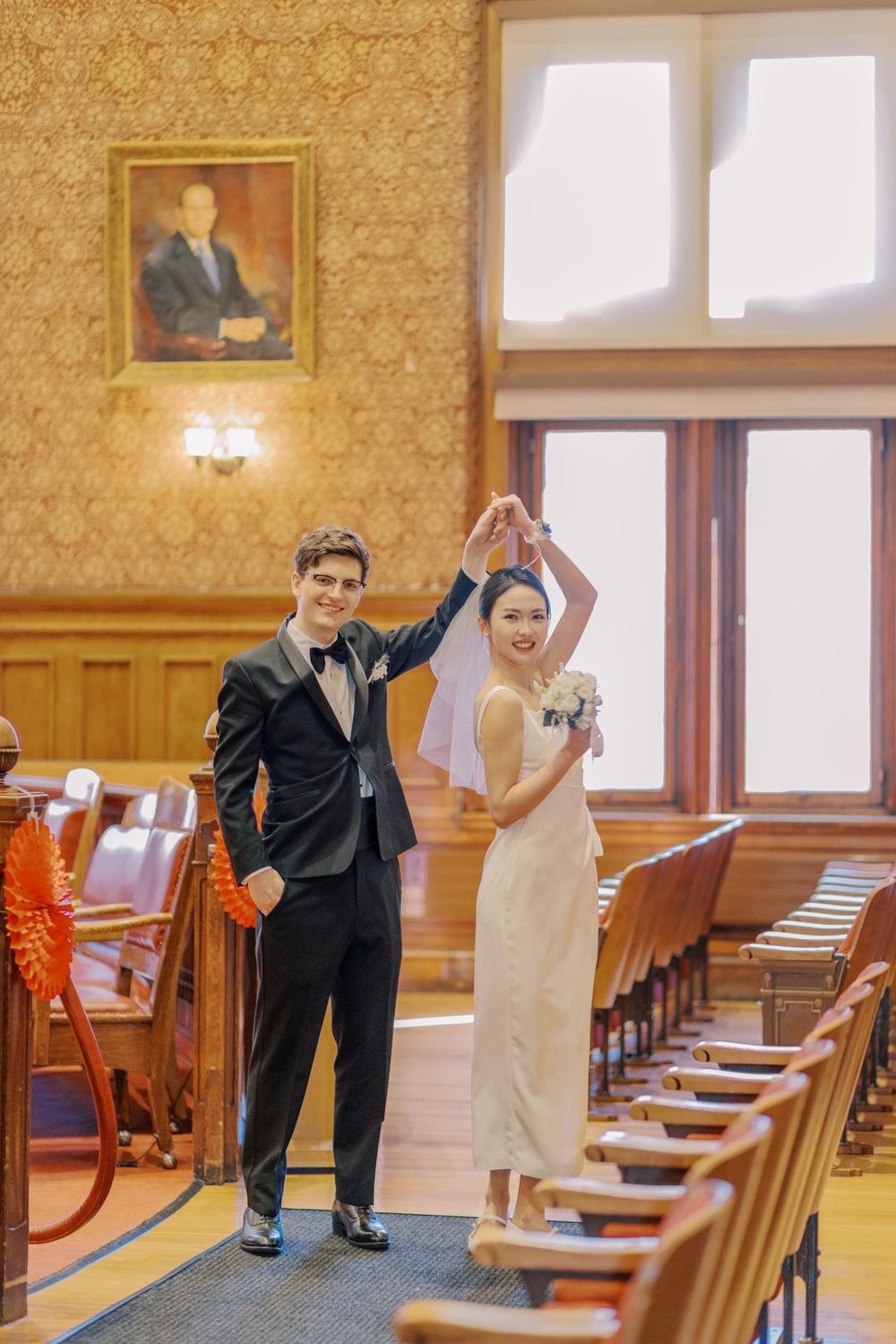 Wedding couple dances and poses playfully in an ornate hall with vintage wood details.