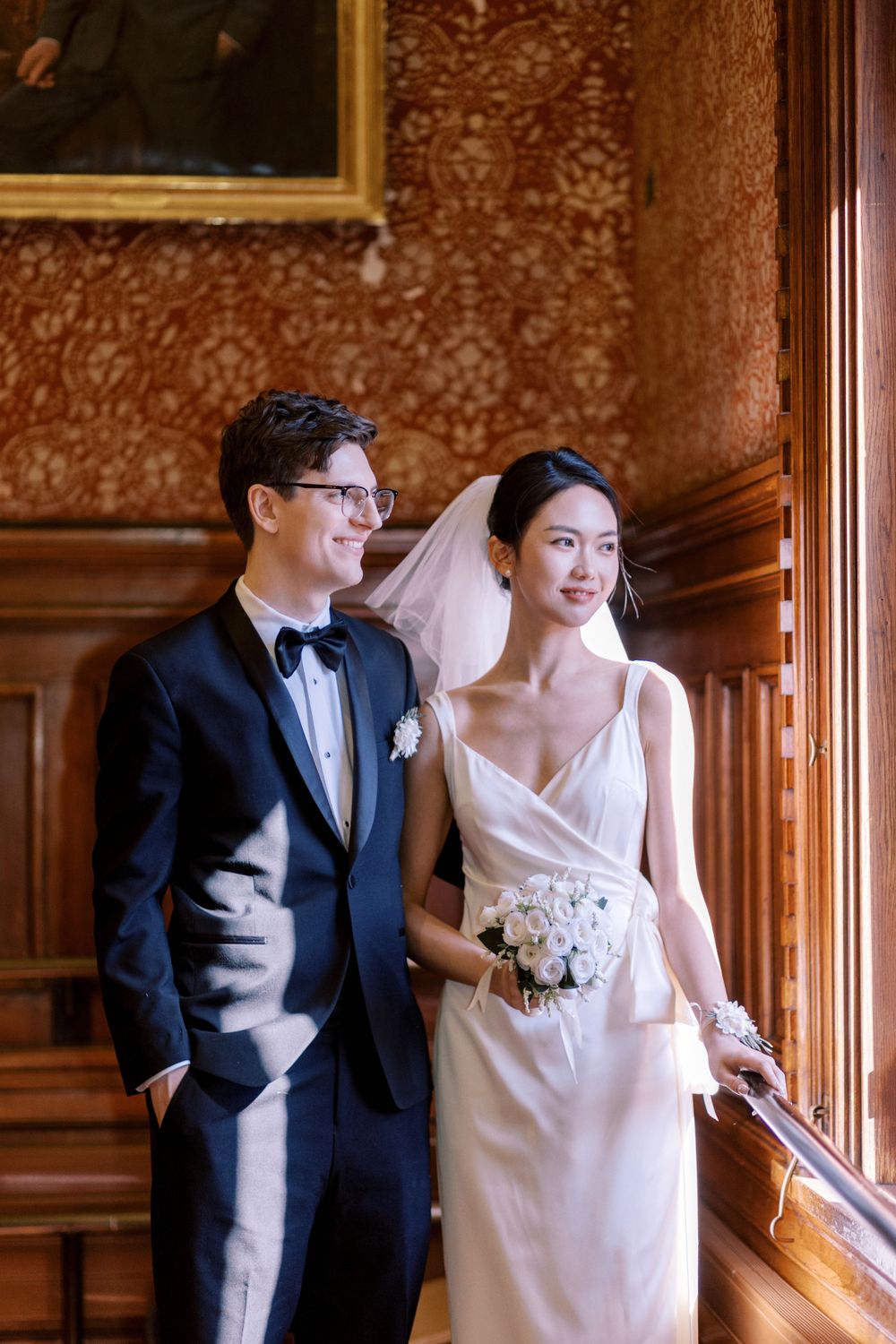 Newlyweds pose together along wooden wall panels in an elegant vintage setting.