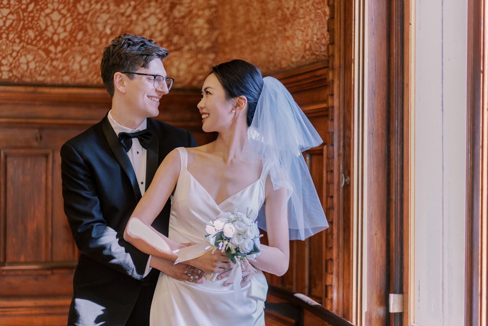 Wedding couple embraces in a classic wood-paneled hallway with ornate details.