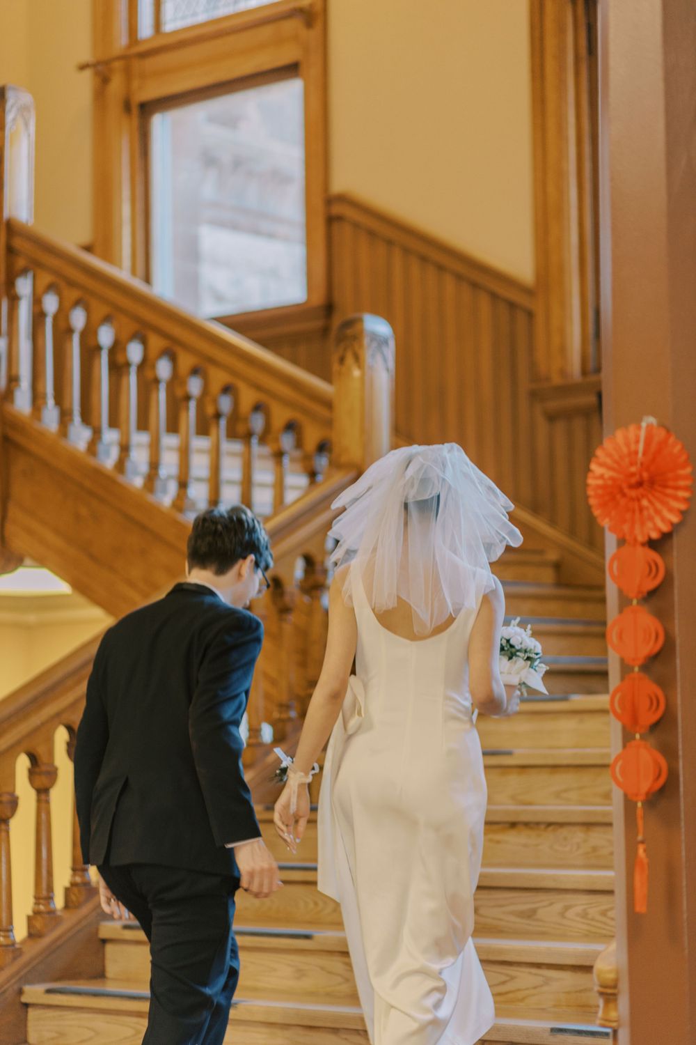 Couple shares a playful moment on an elegant wooden staircase with orange paper decorations.