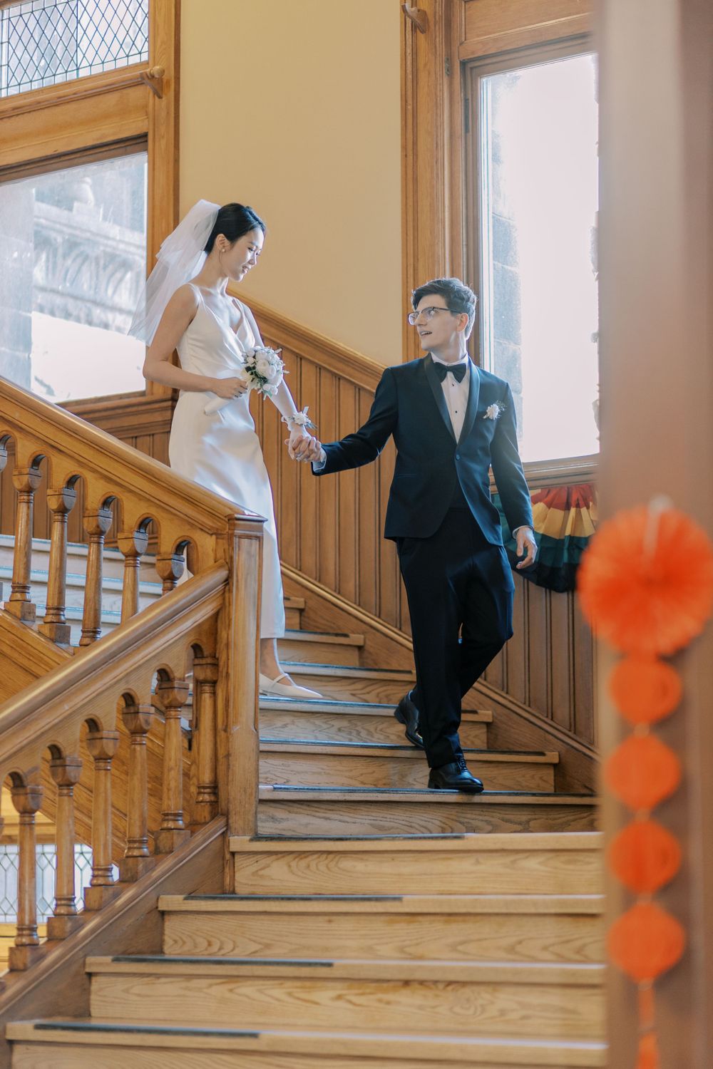 Bride and groom pose on a vintage wooden staircase with orange floral accents.