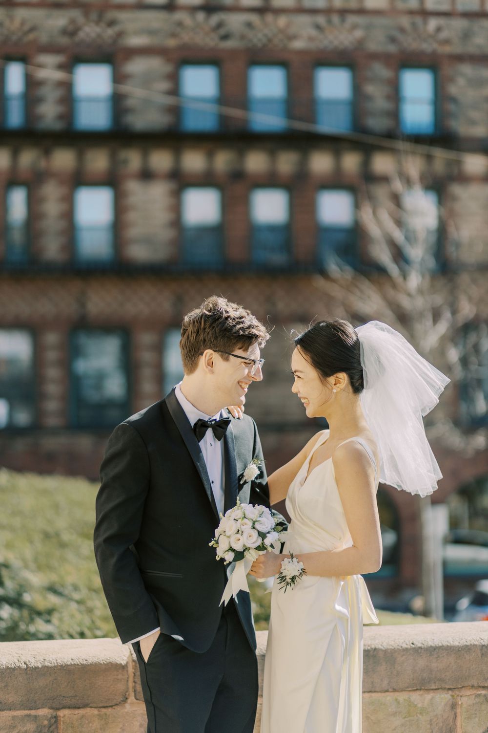 Wedding couple shares intimate moments against brick building backdrop on sunny day.