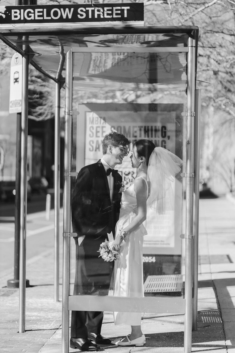 Newlyweds pose romantically at Bigelow Street bus stop in black and white photo.