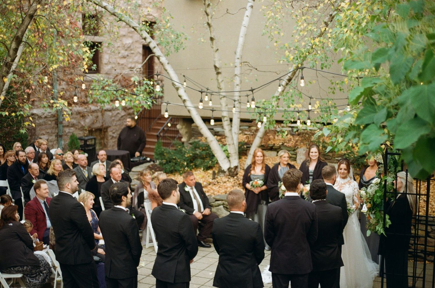 photo of the wedding party standing by the bride and groom as they are saying their vows, on film