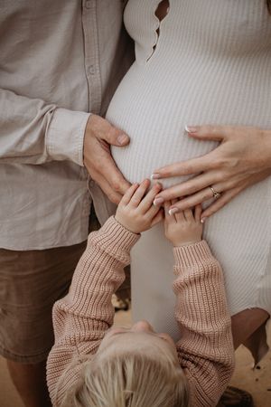 Close up of mum, dad and daughter touching mum's pregnant belly.