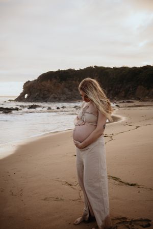 Mum looking down at pregnant belly at the beach.