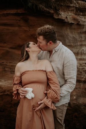 A couple kissing while holding wifes pregant belly and little baby booties.