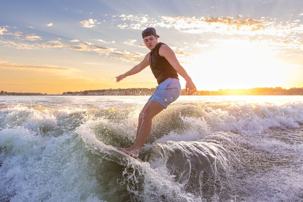 Surfer rides a wave at sunset creating dramatic splashes and silhouette against the golden sky at West Okoboji Lake.
