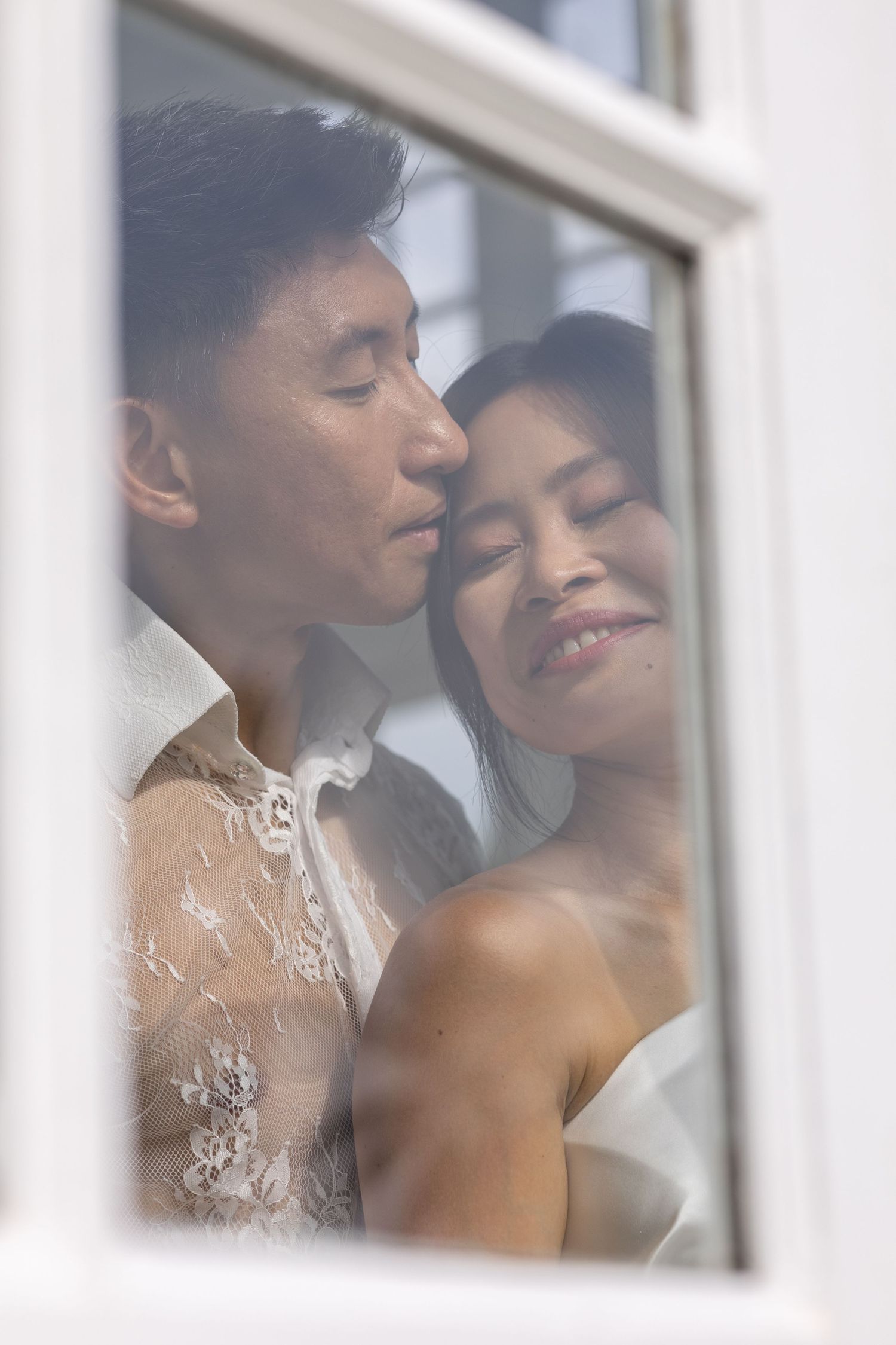 A romantic couple shares an intimate moment through a window, their silhouettes softly lit and faces close together.