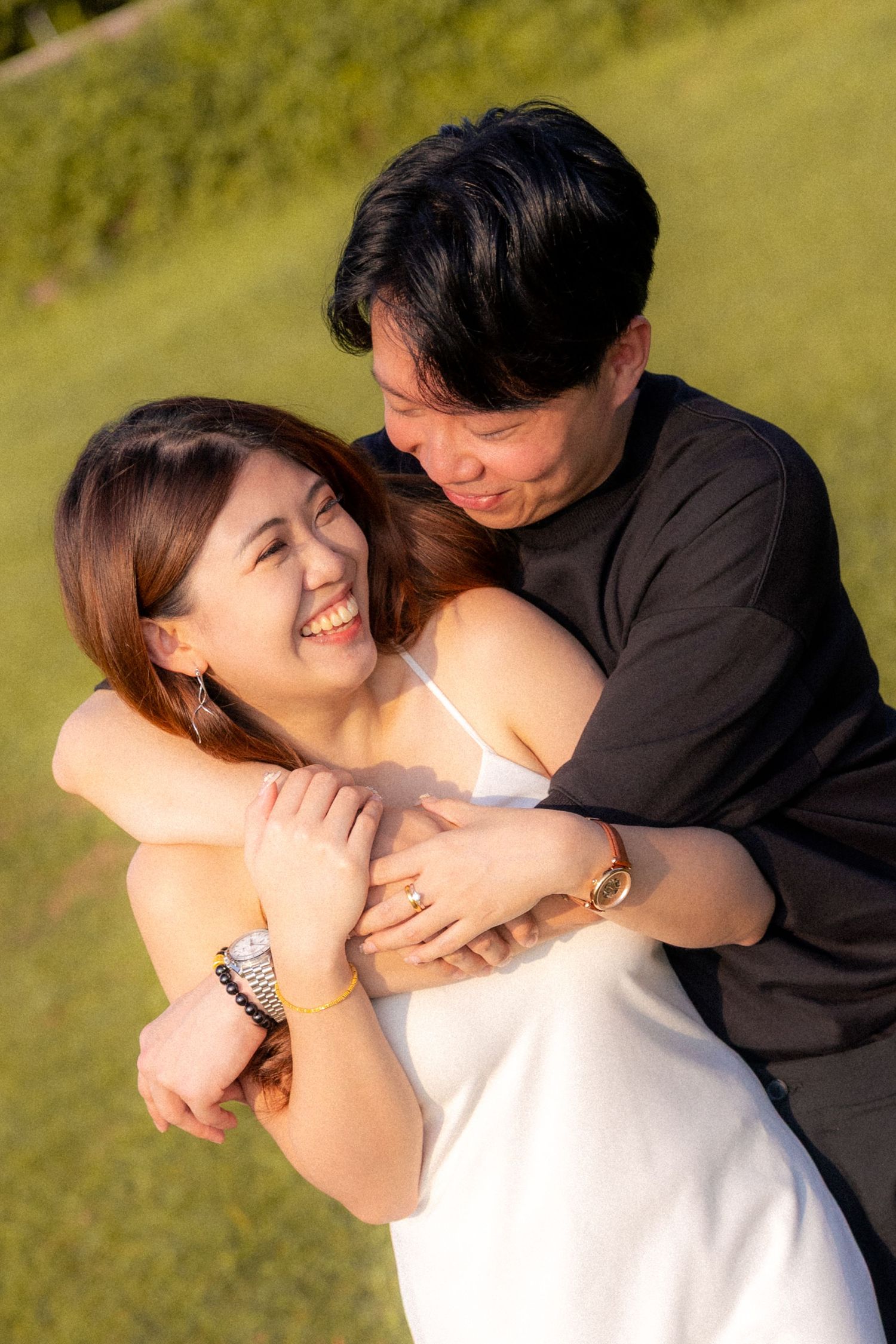 A couple embraces in a series of candid romantic moments on a sunny grassy hillside.