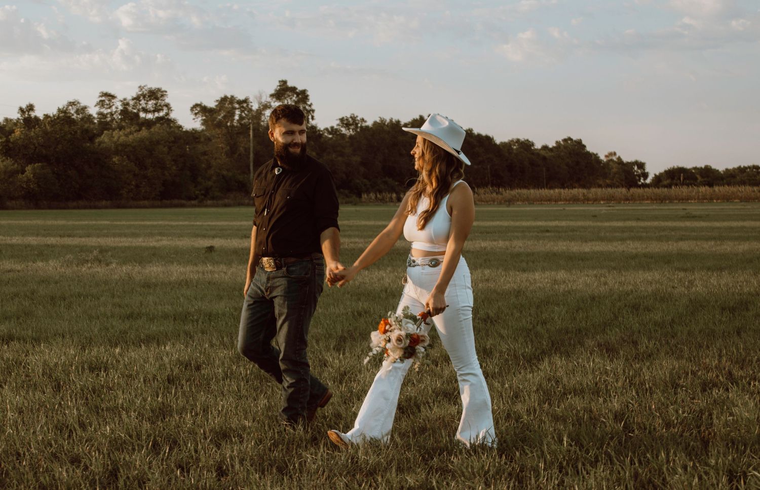 A couple walking hand in hand through a golden meadow at sunset.