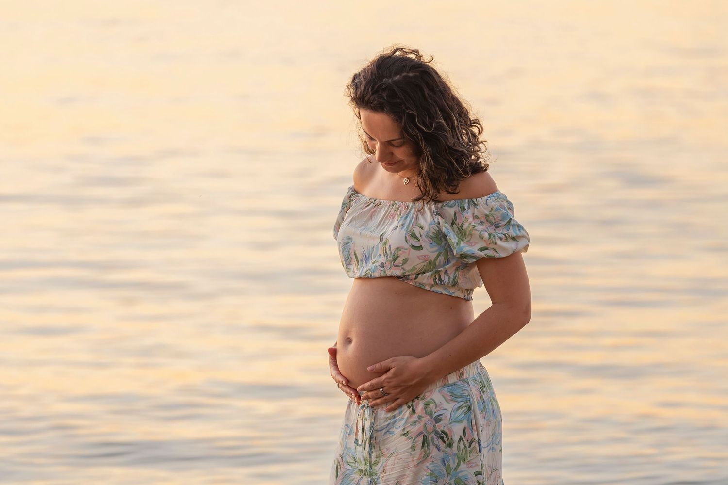 Silhouette of pregnant woman at sunset by the water.