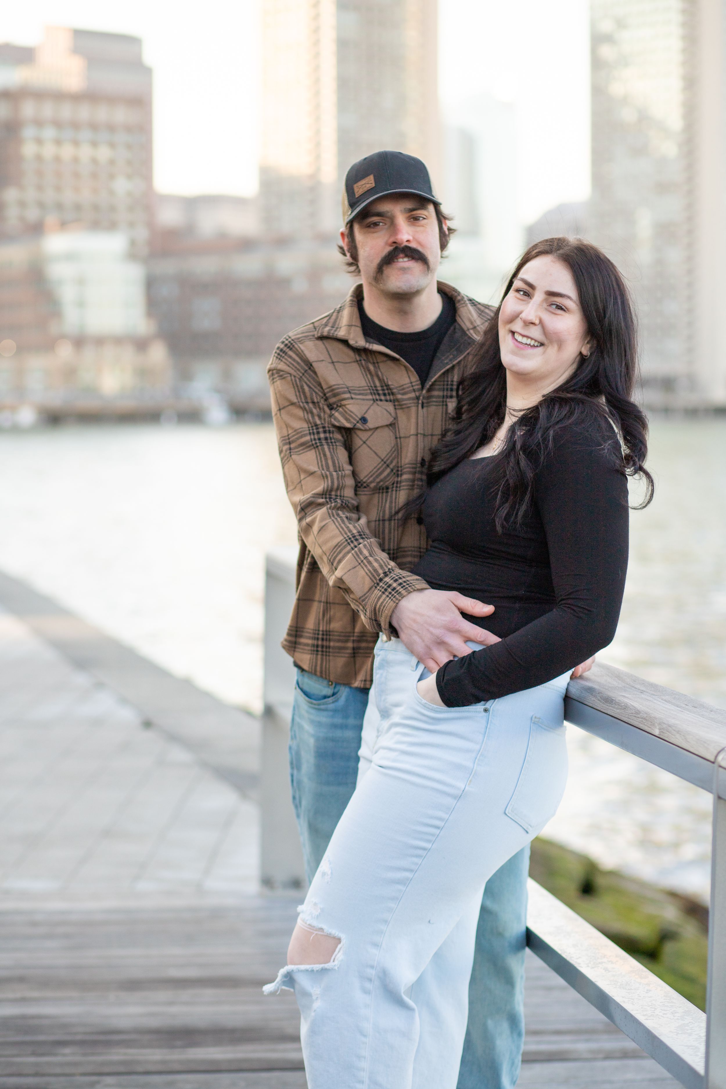 photoshoot in boston seaport; couple walks along fan pier park with boston in the background