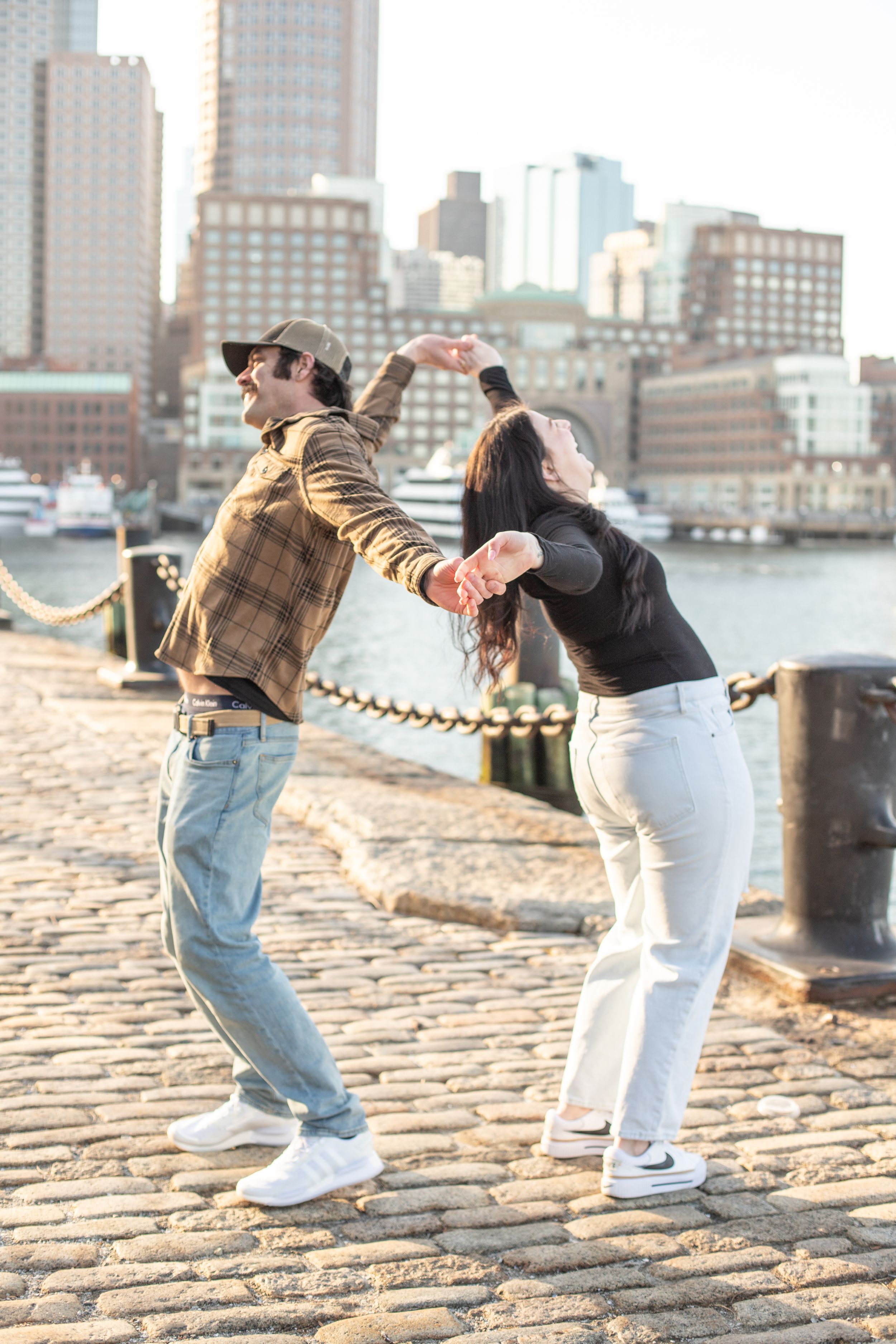 photoshoot in boston seaport; couple dances along fan pier park with boston in the background; candid lifestyle shoot