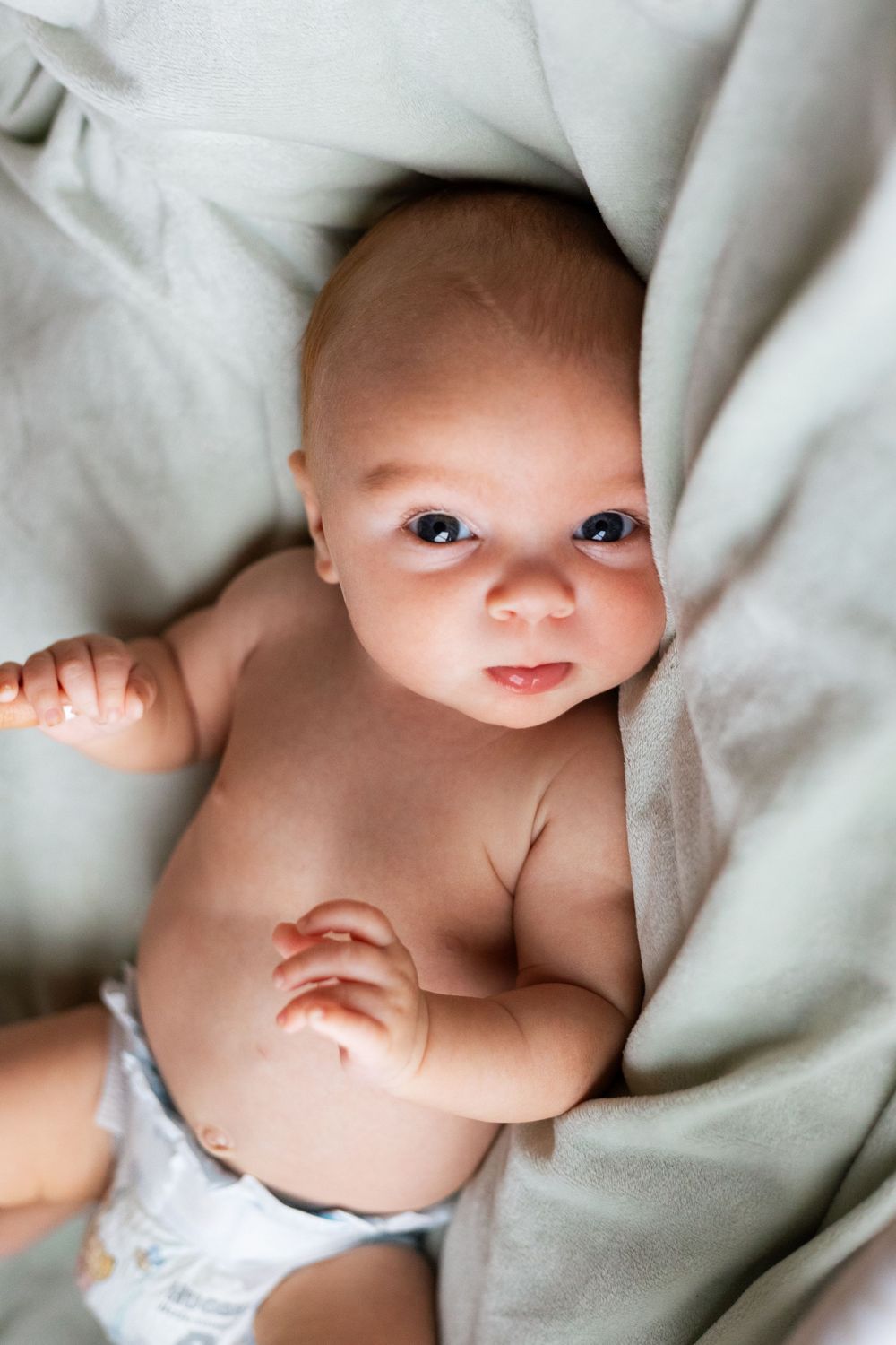 Sweet photos of an infant lying on soft gray bedding looking at the camera.