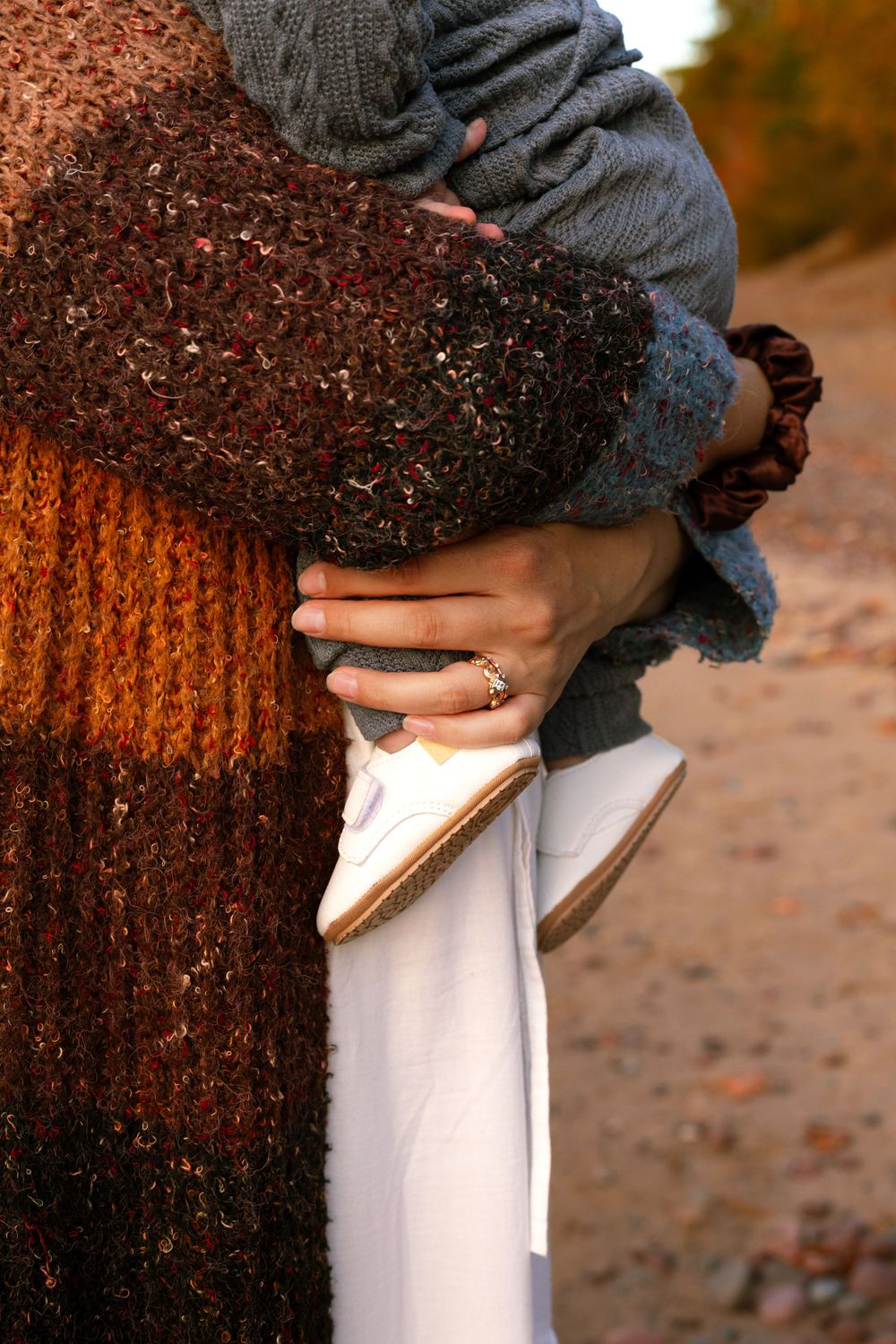 Close-up details of gray sweater and white pants against autumn textures.
