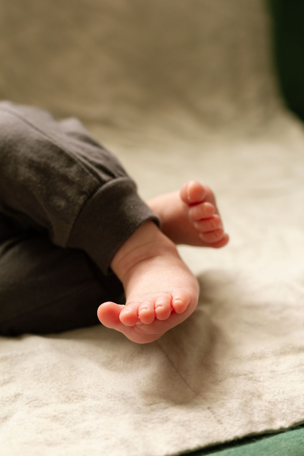 Close-up of tiny newborn baby feet wearing dark gray pants, resting on a soft light blanket.