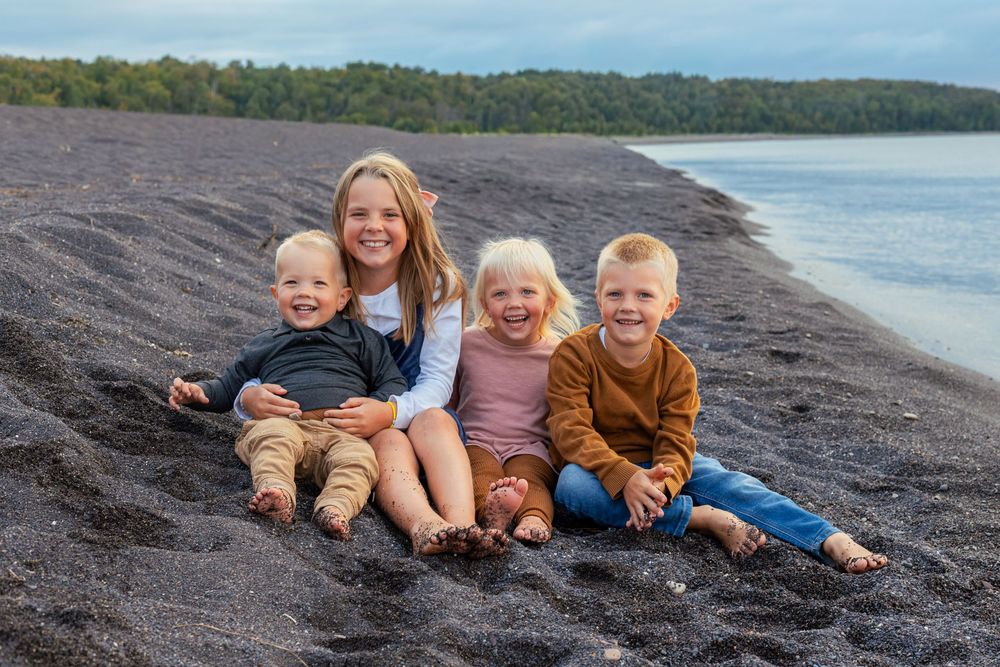 Group sitting together on a black sand beach with ocean and trees in background.