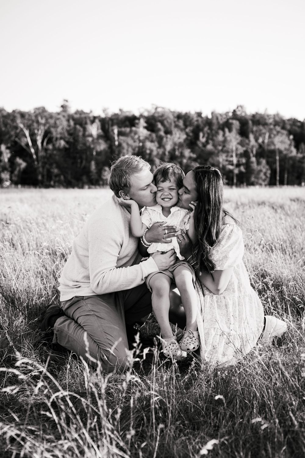 A tender family moment captured in black and white in a sunlit meadow.