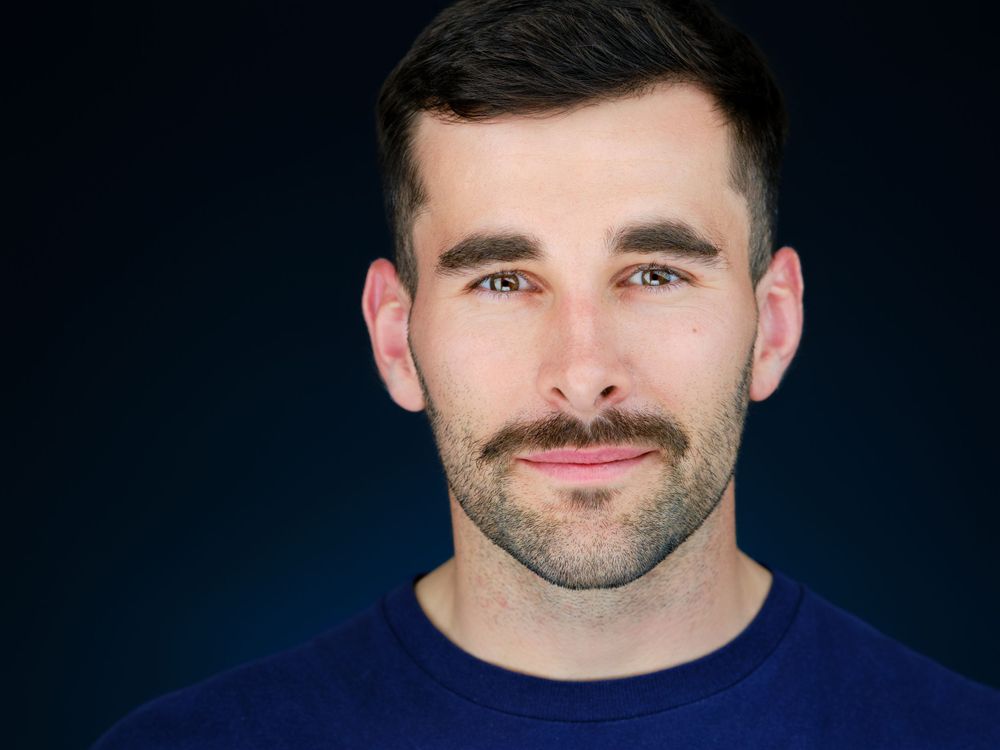 Professional headshot of smiling man with beard wearing blue shirt.