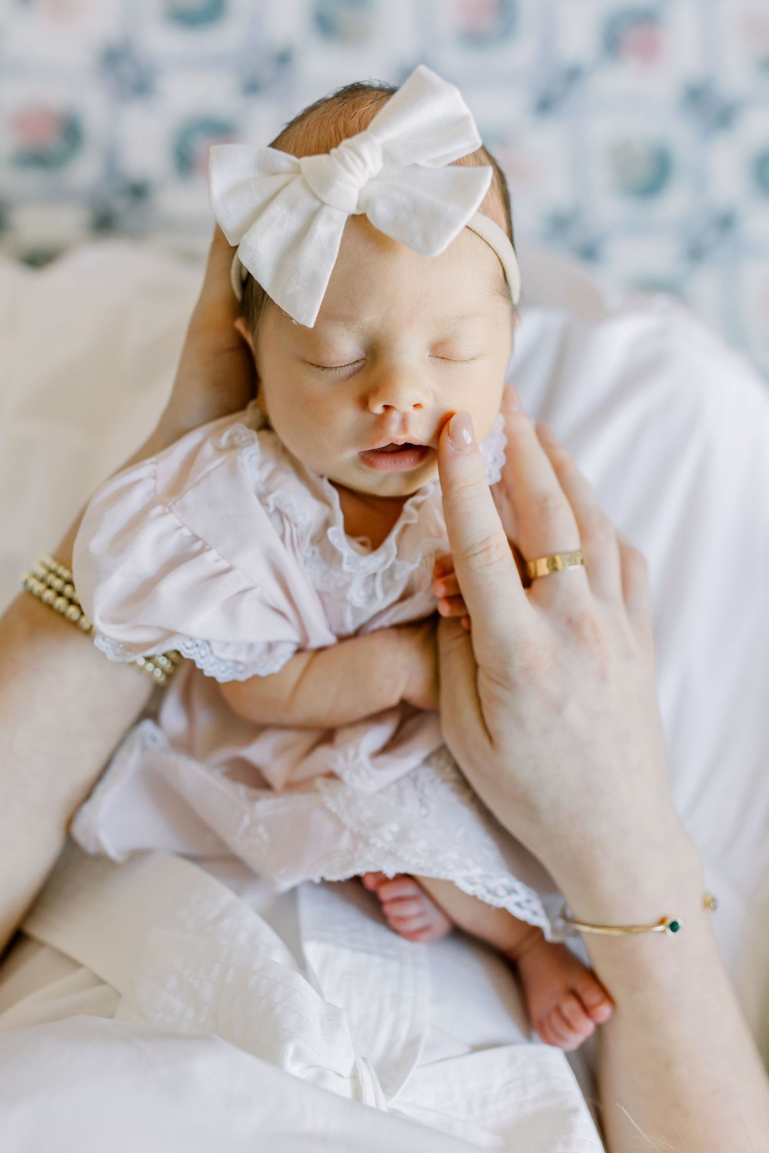 Sleeping baby in white dress and bow headband lying on plush white fabric.