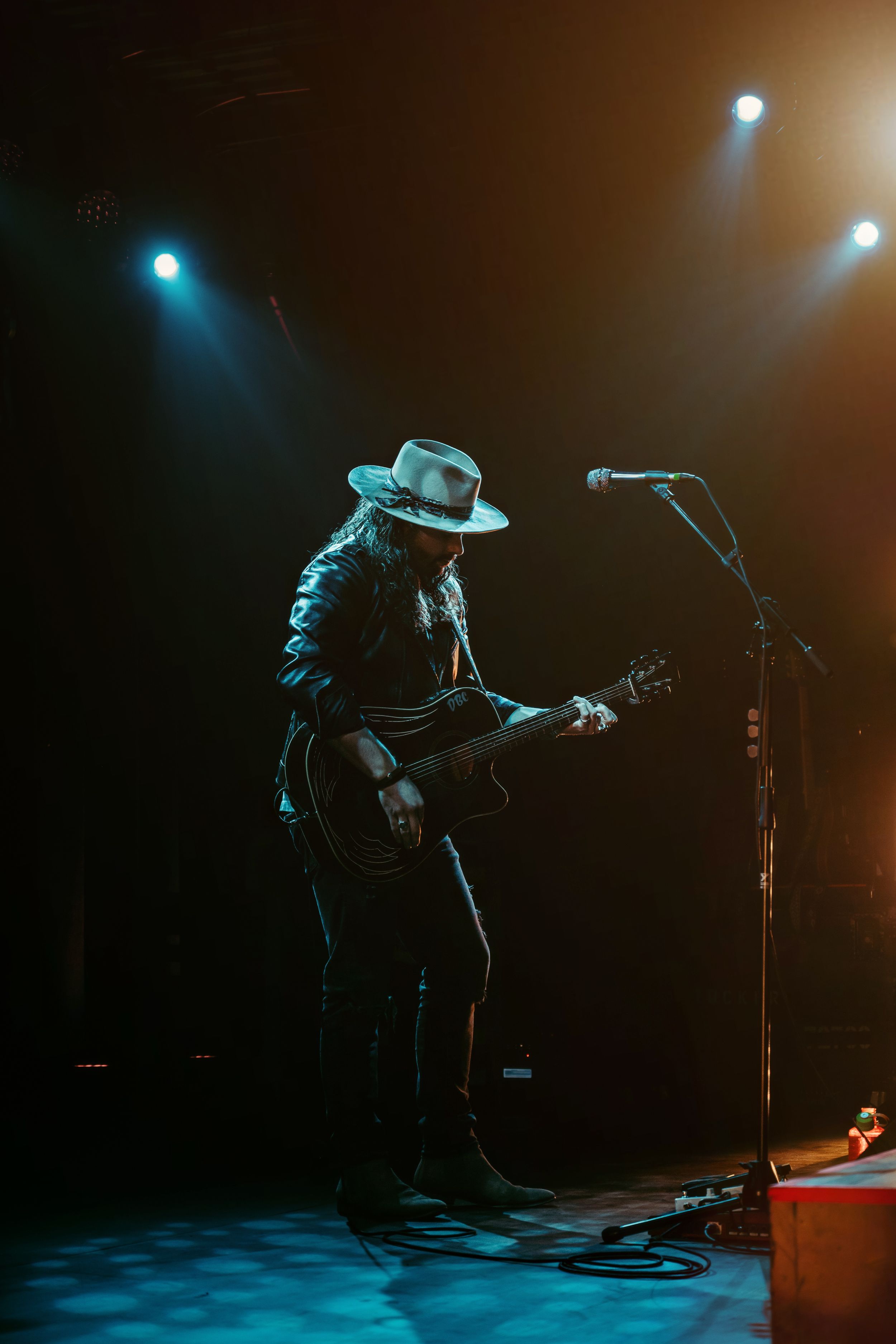 Silhouetted guitarist in a cowboy hat performs on a dimly lit stage with blue spotlights.