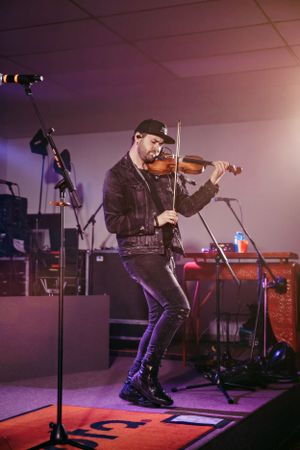 Violinist performs energetically on stage under purple lighting.