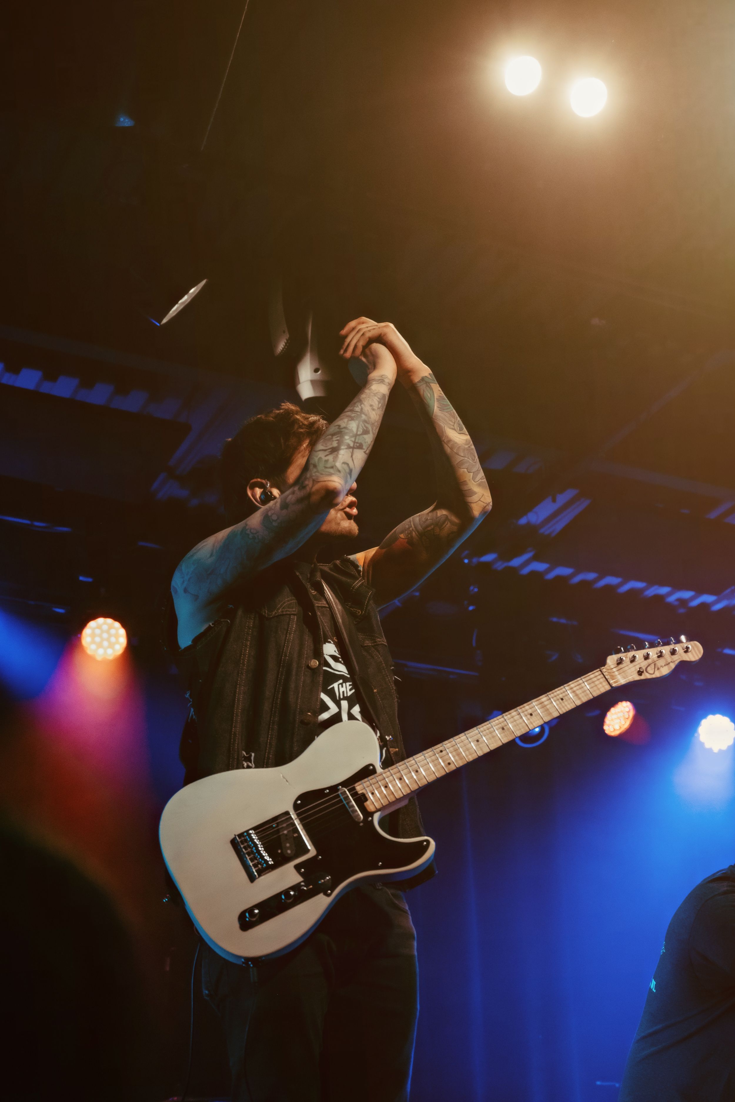 Energetic musician performing with a silver electric guitar under dramatic blue stage lighting.