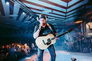 Acoustic guitarist performs under geometric ceiling patterns with blue lighting.
