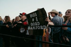 Concert crowd at a music festival holding up a black banner or flag near the front barrier.