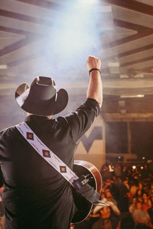 Country musician raises arm while performing with guitar to crowded venue.