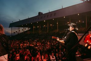 Country music performance at historic racetrack with grandstand visible in twilight.