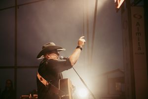 Concert performer raises arm during dramatic backlit performance on stage.