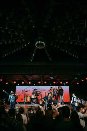 Musical performance on stage with band members and red backdrop lighting during a live concert at an indoor venue.