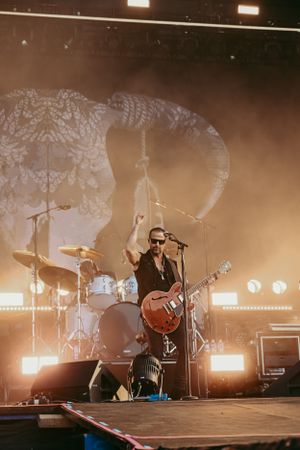Guitarist performs on stage with dramatic backlighting and smoke effects.