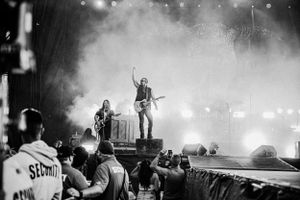 Black and white concert photo showing performers on stage with crowd and dramatic lighting.