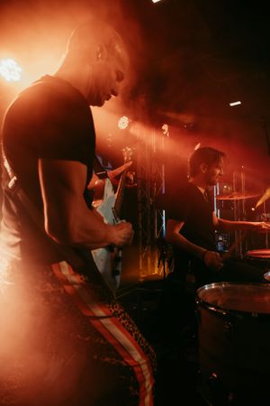 Musicians perform on stage with dramatic orange lighting and smoke effects.