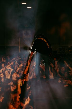 Concert performer leans over stage edge during high-energy performance with crowd reaching up in smoky atmosphere.