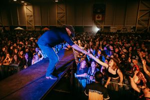 Performer in blue reaches out to energetic crowd during intense concert performance.