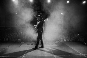 Silhouetted guitarist performs on smoky stage with dramatic lighting.